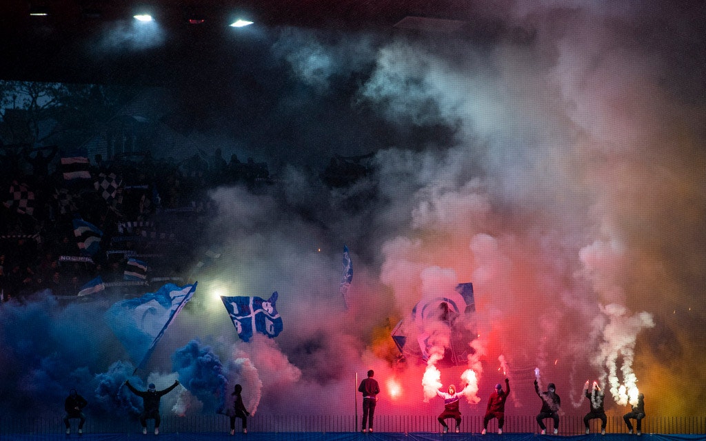 Des supporters allument des engins pyrotechniques pendant un match de football.